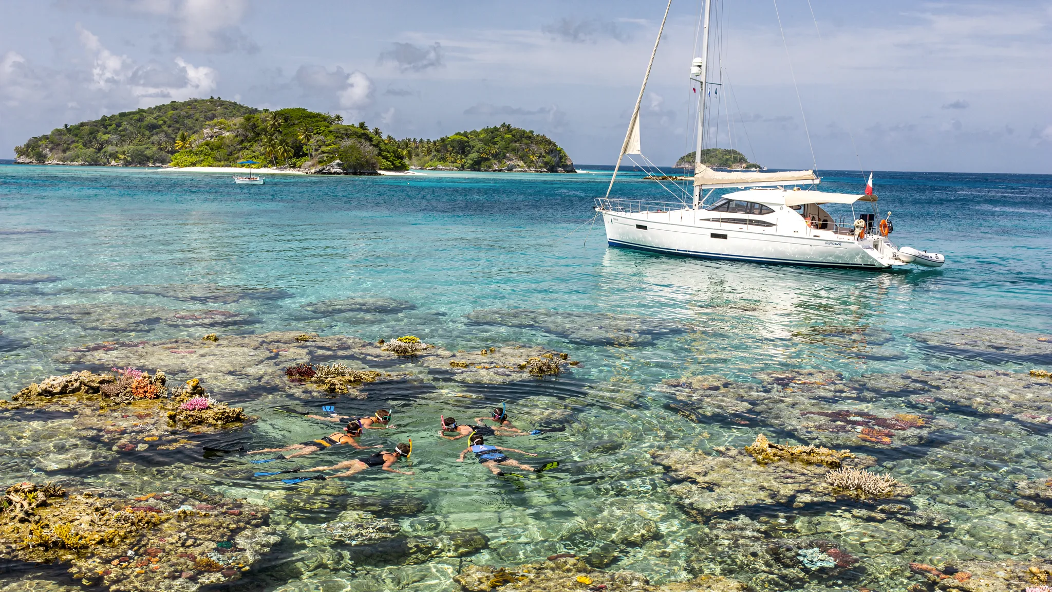 A serene lagoon scene in the Tobago Cays with a luxury yacht at anchor in turquoise water, small uninhabited islets in the background, and snorkelers near a shallow coral reef.
