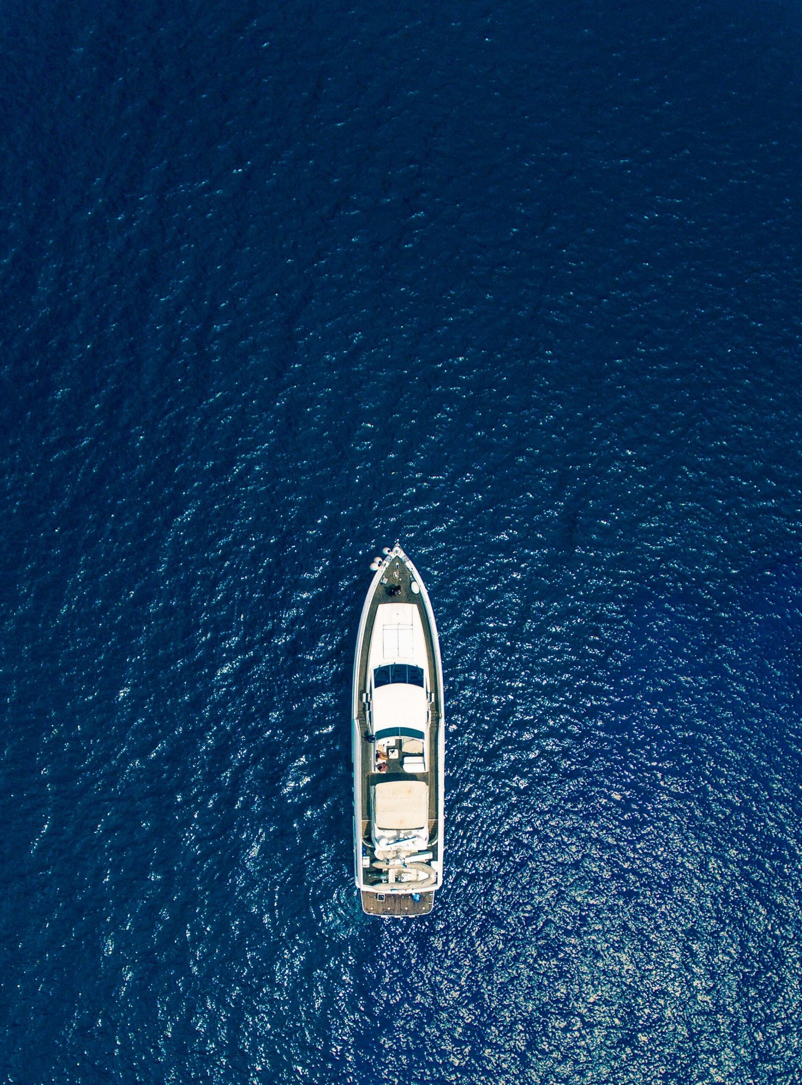 A sleek white motor yacht anchored on crystal-clear turquoise Mediterranean sea with calm blue water surrounding it