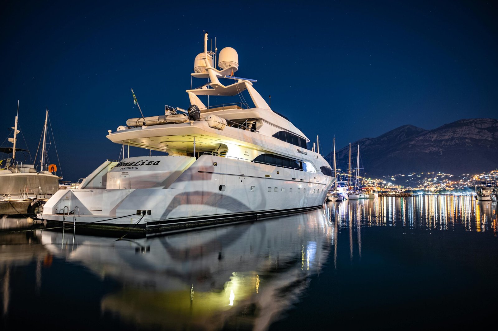 An elegant yacht illuminated at night moored on a calm, dark sea reflecting warm cabin lights