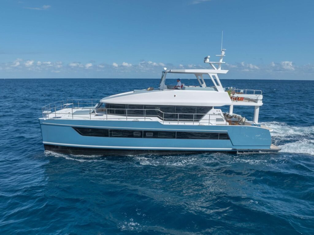 White luxury yacht sailing on a calm blue sea under a clear sky, viewed from the side with open deck areas and railings.