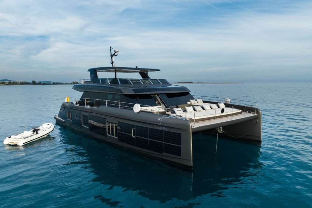 Luxurious catamaran yacht anchored in calm blue water with a small dinghy nearby.