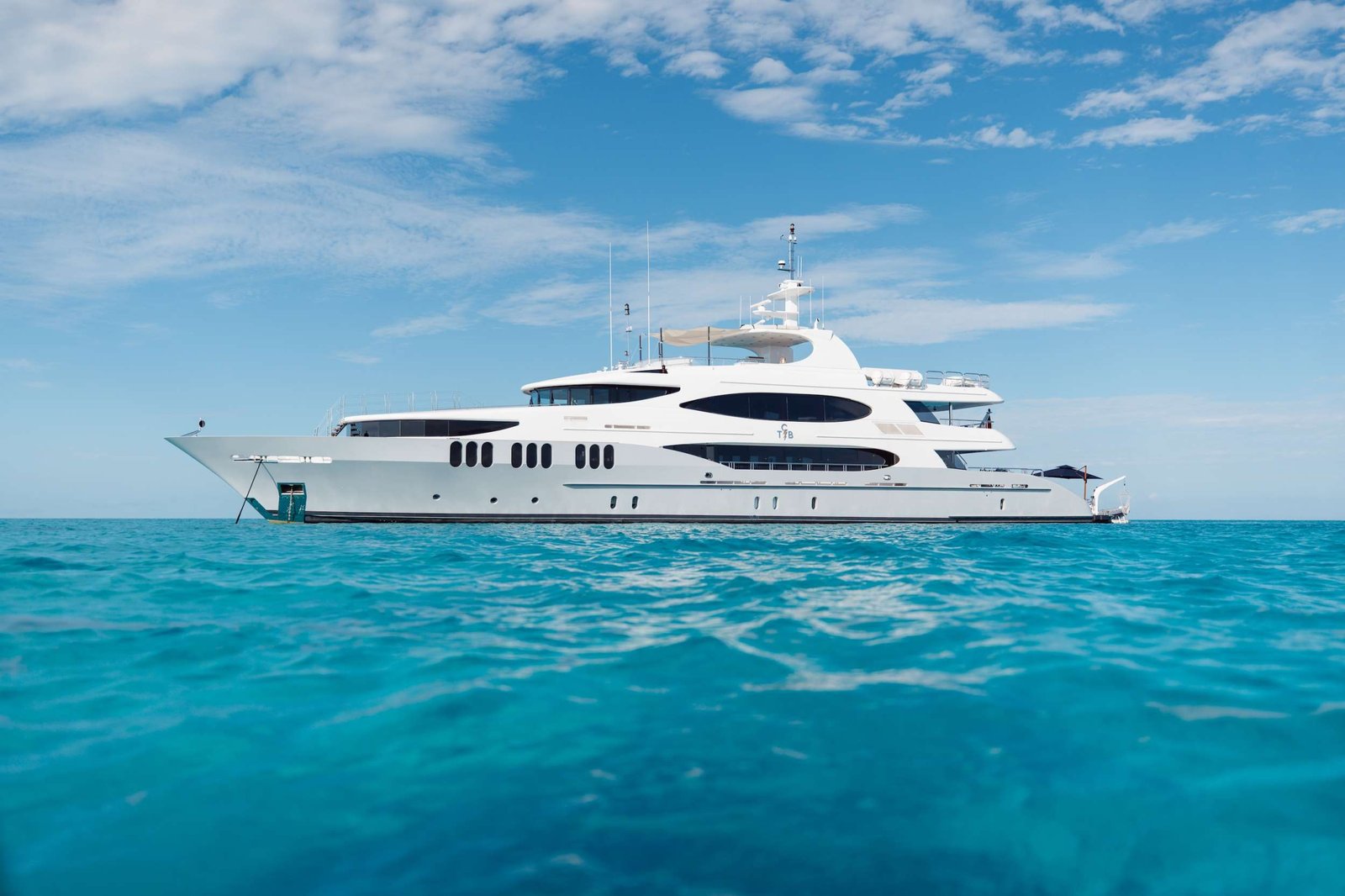 White luxury motor yacht cruising on calm turquoise sea under a clear blue sky.