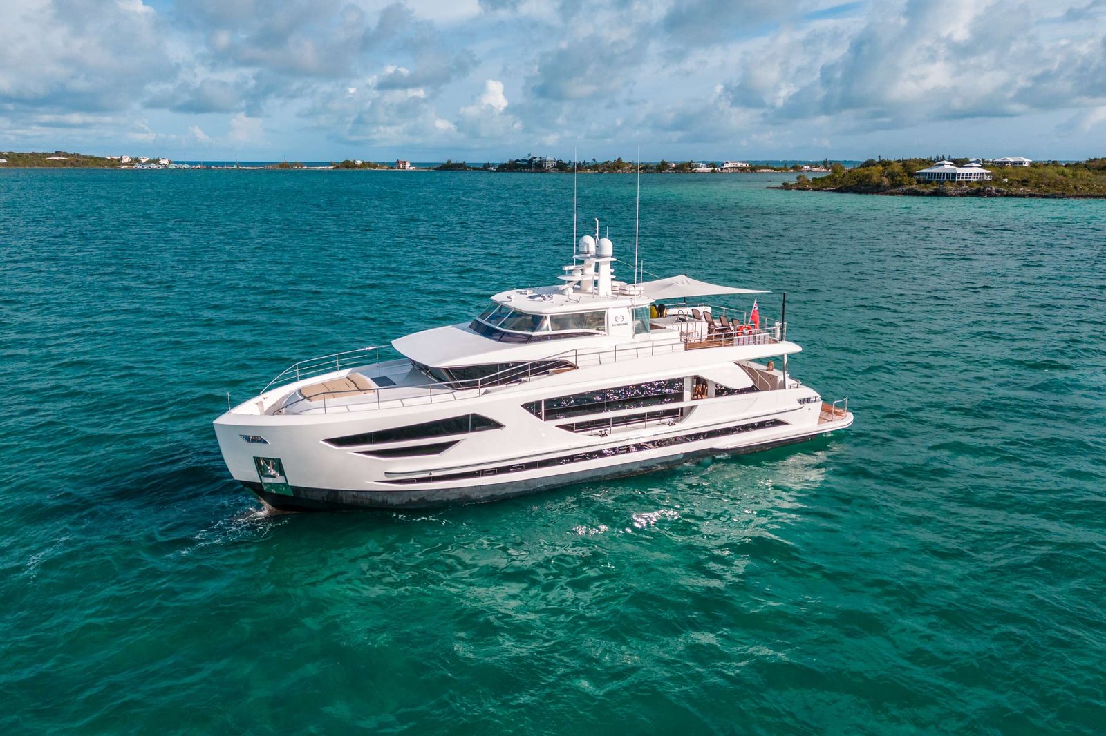 White luxury yacht cruising on turquoise sea with a distant coastline and cloudy sky above