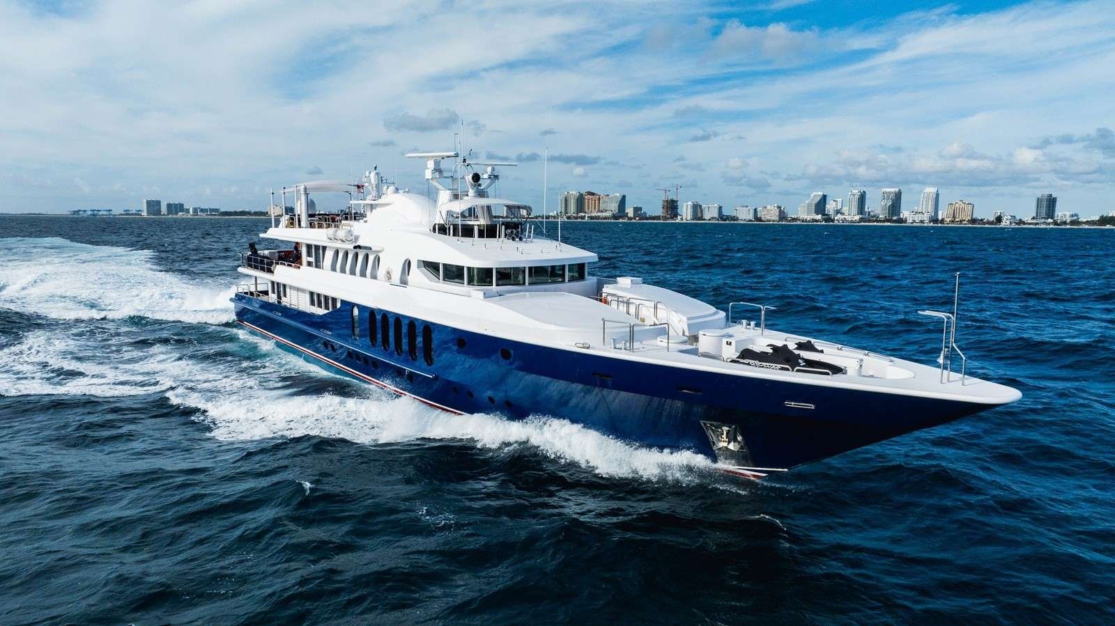 Luxury white and blue motor yacht cruising on deep blue water with a city skyline in the distance
