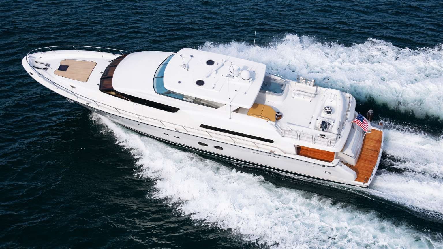 White luxury motor yacht cruising at speed on dark blue ocean, sending white wake behind it.
