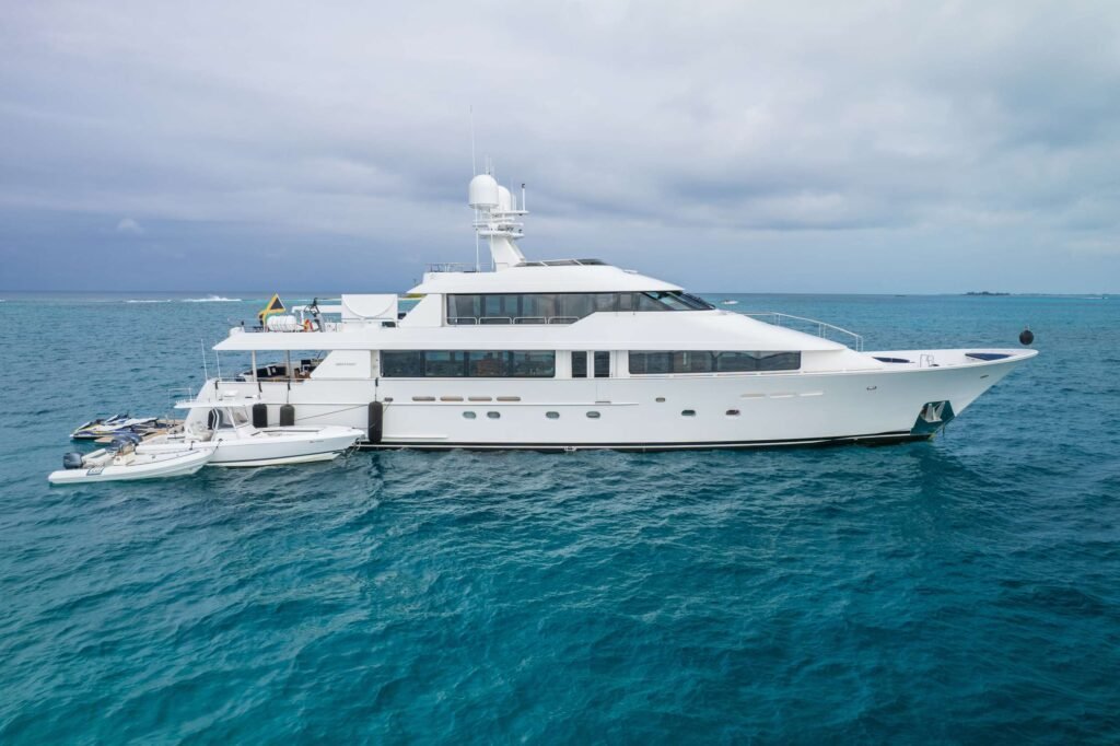 White luxury yacht anchored in turquoise sea under a cloudy sky, with small boats nearby.