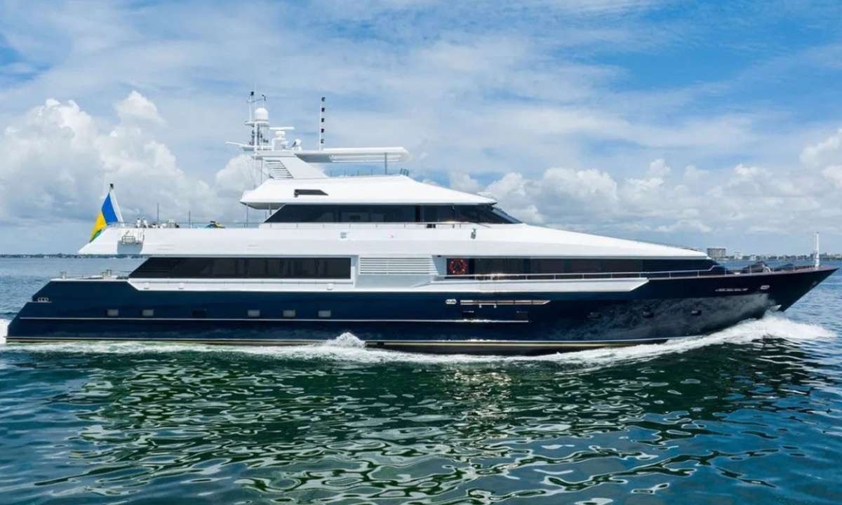 Luxury motor yacht cruising on calm blue water, Ukrainian flag at the stern amid a sunny sky.