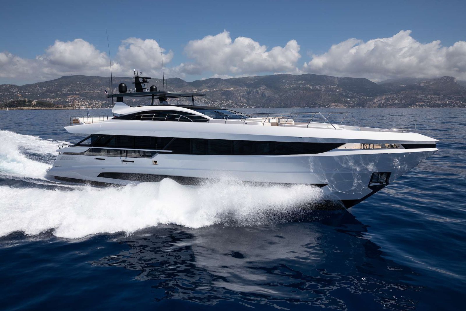 White luxury motor yacht speeding across blue sea with wake of waves and distant mountains