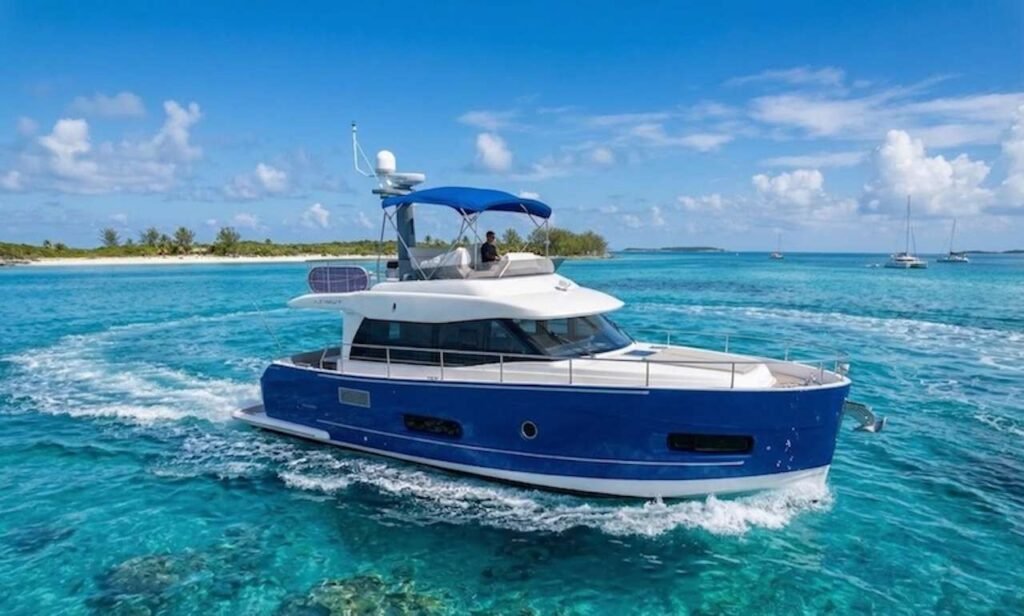 Blue-and-white motor yacht cruising through turquoise tropical water with a white sandy island and palm trees in the background.