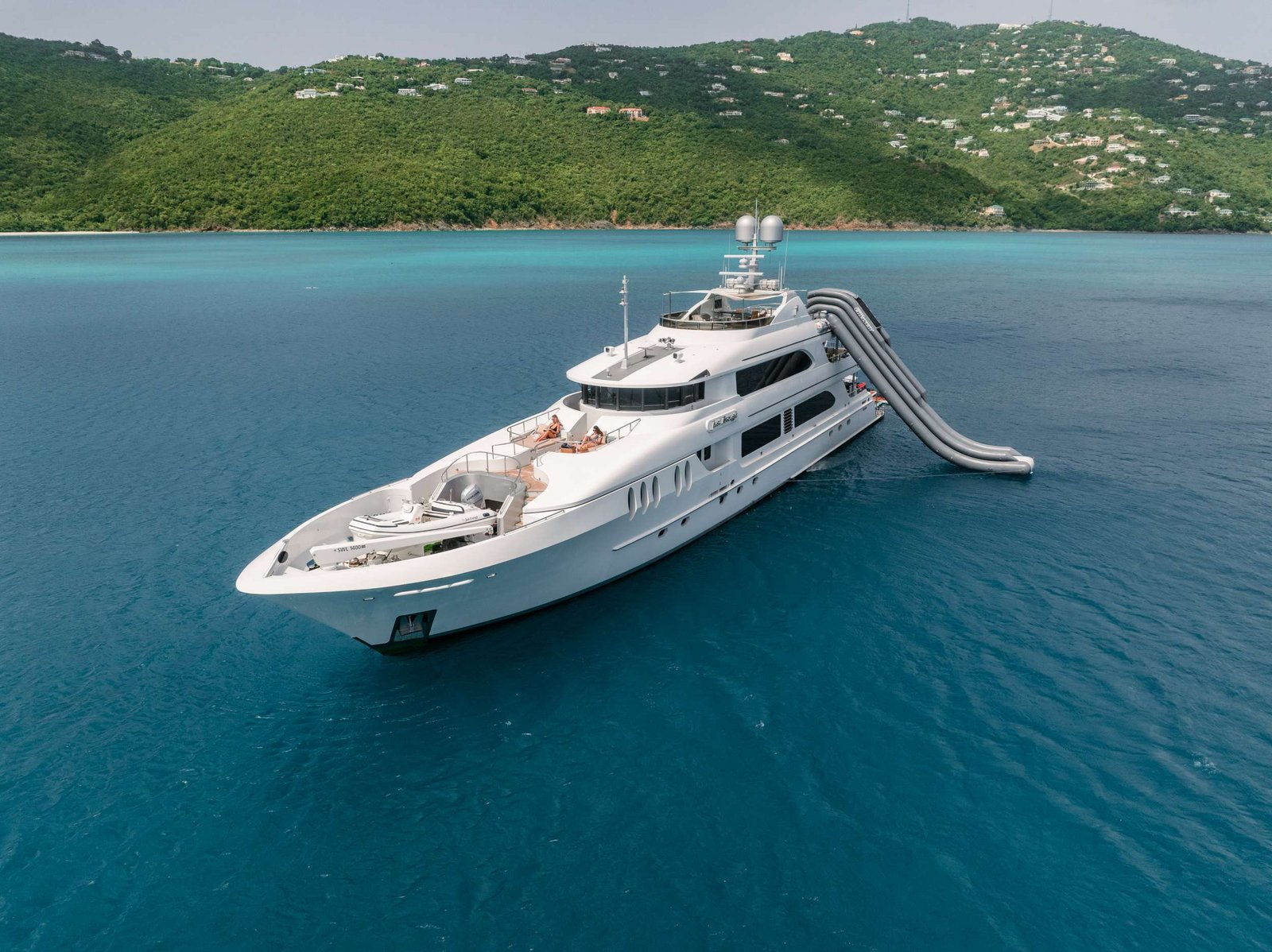 White luxury yacht on turquoise sea with green, hilly island in the background.