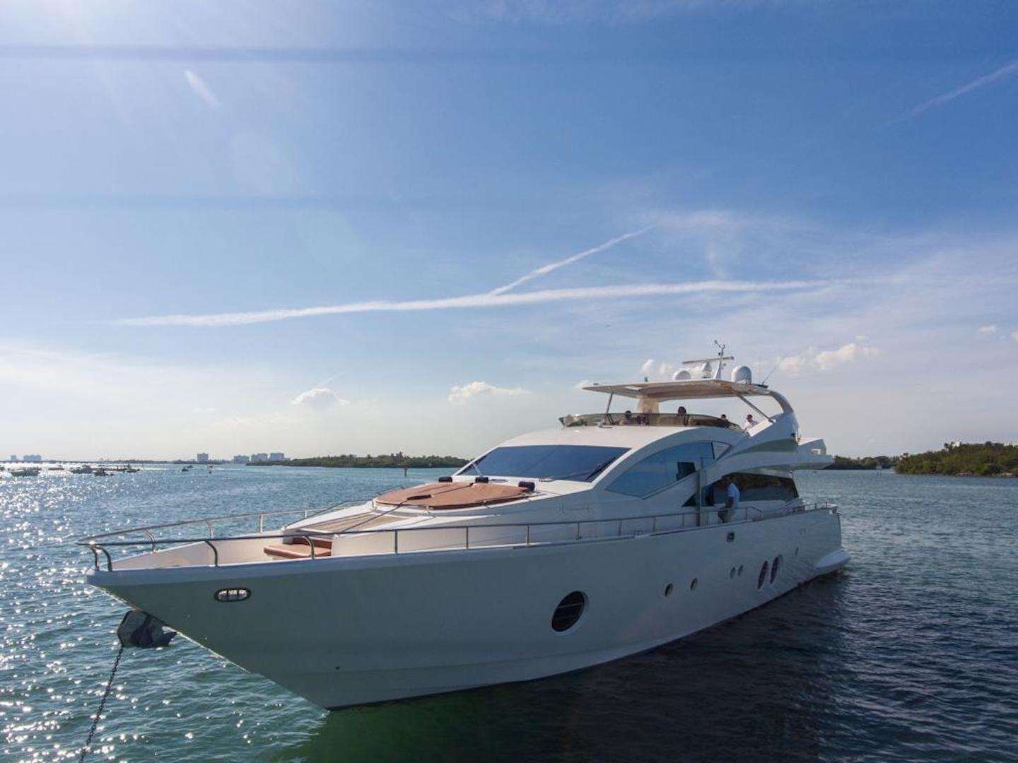 Luxurious white motor yacht anchored on calm blue water under a clear sky and sun glare.