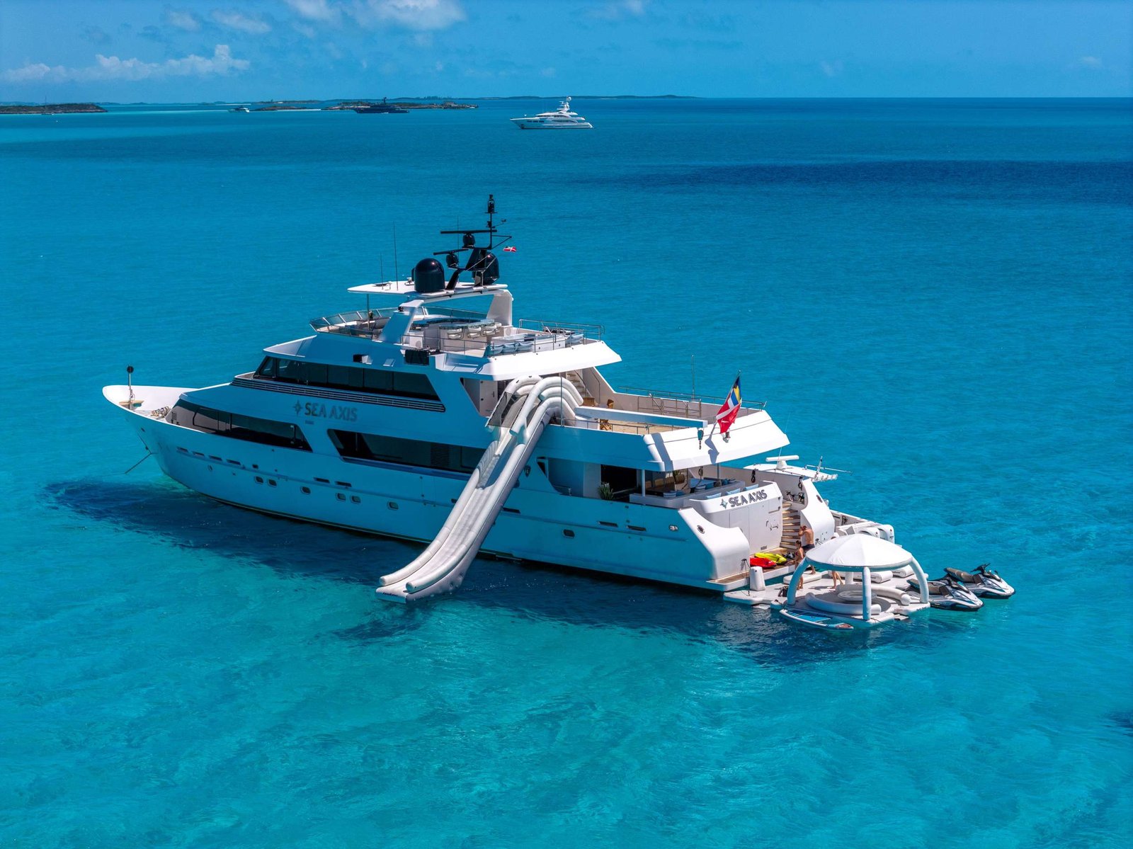 White luxury yacht anchored in turquoise sea with a curved water slide extending into the water at the stern of the boat.