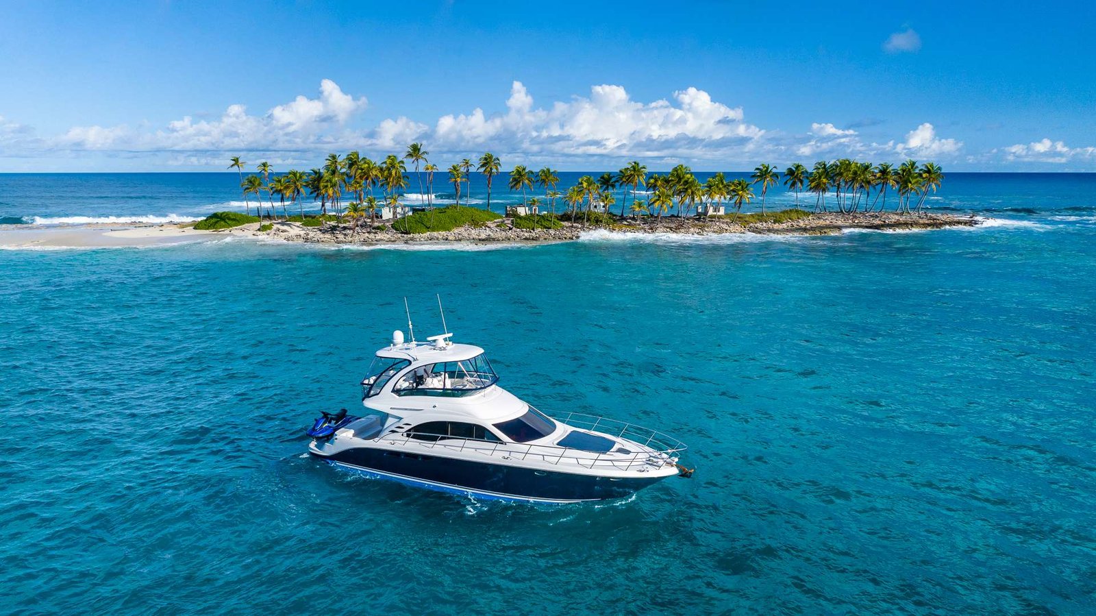 White luxury yacht on bright blue tropical sea near a palm-covered island and sandy shore under a clear sky