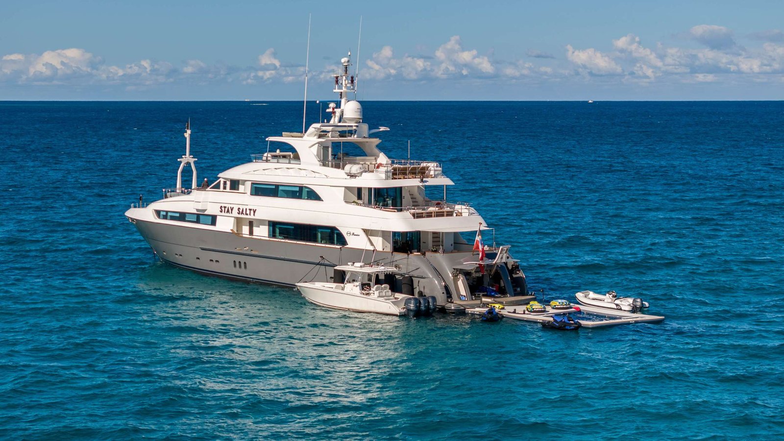 White luxury yacht named Stay Salty anchored in blue tropical water with jet skis alongside.