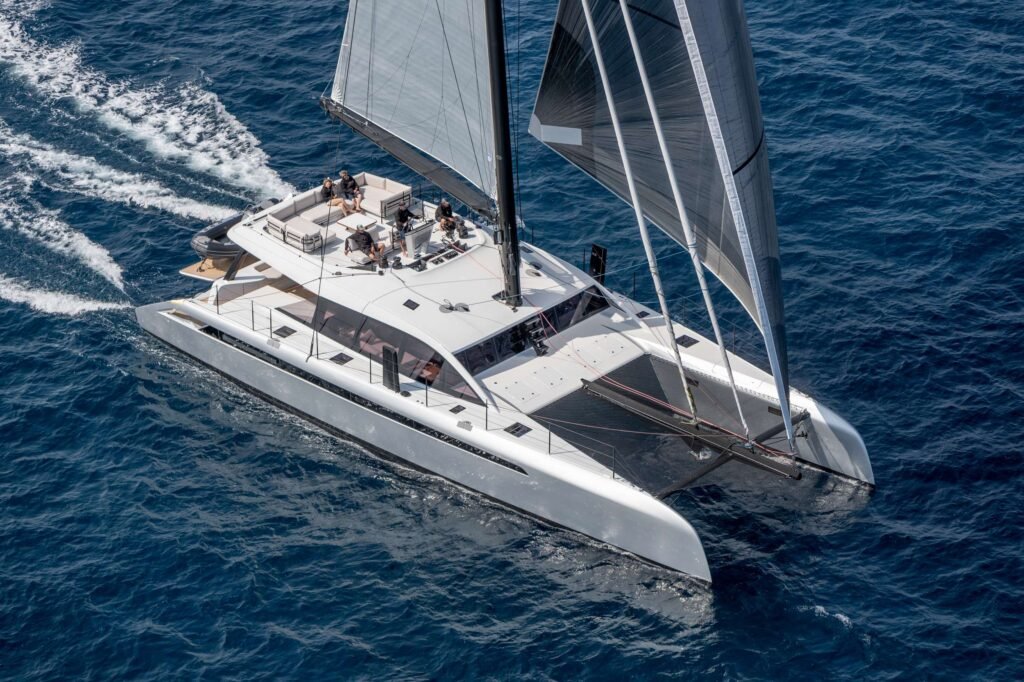 Overhead view of a white catamaran sailing on deep blue ocean with passengers relaxing on the deck