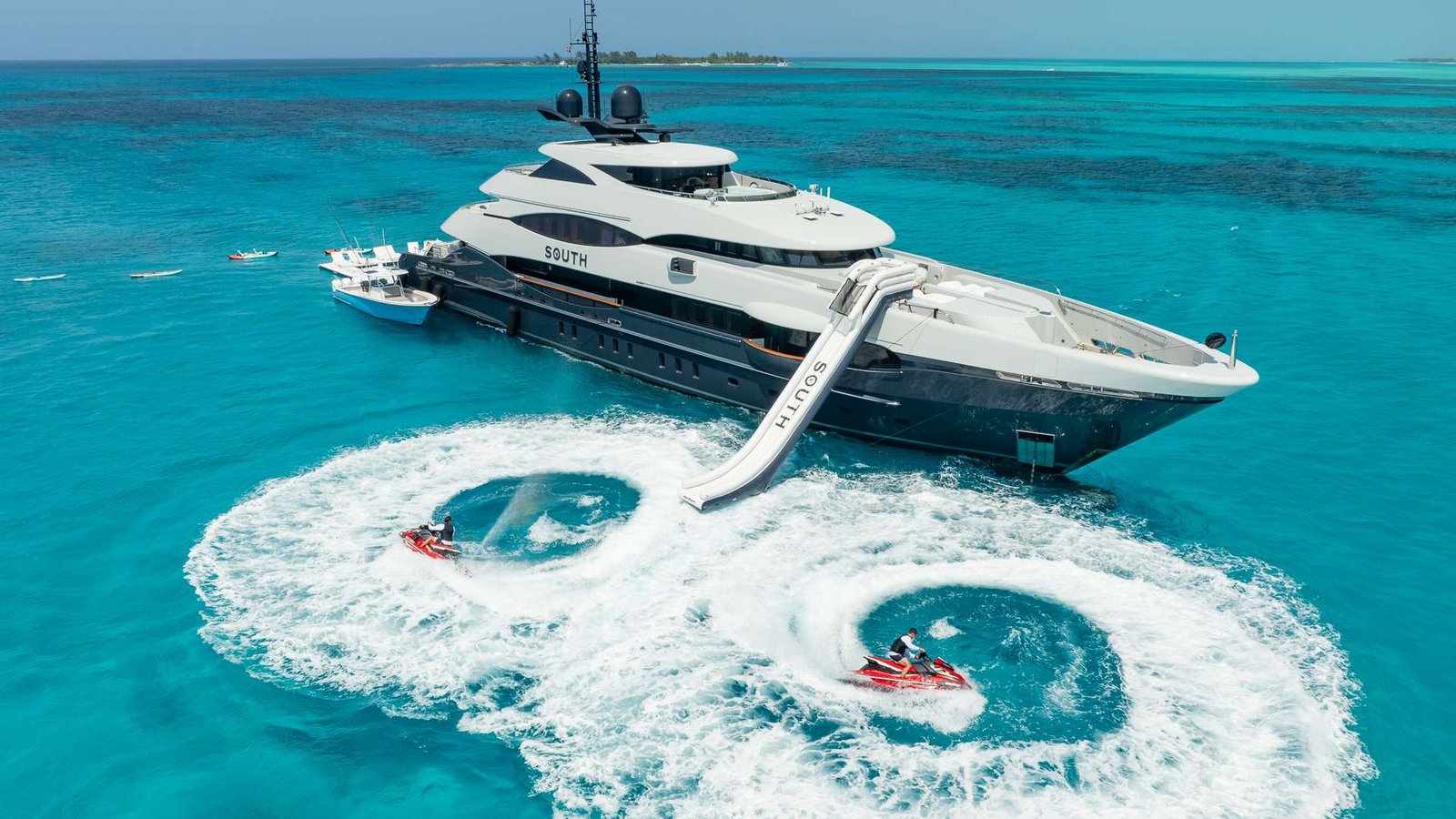 Luxury white motor yacht named South in clear turquoise water with a curved waterslide extending toward the sea.