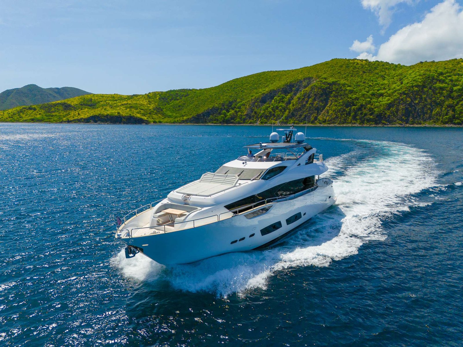 White luxury motor yacht speeding across blue ocean with green hillside in the background.