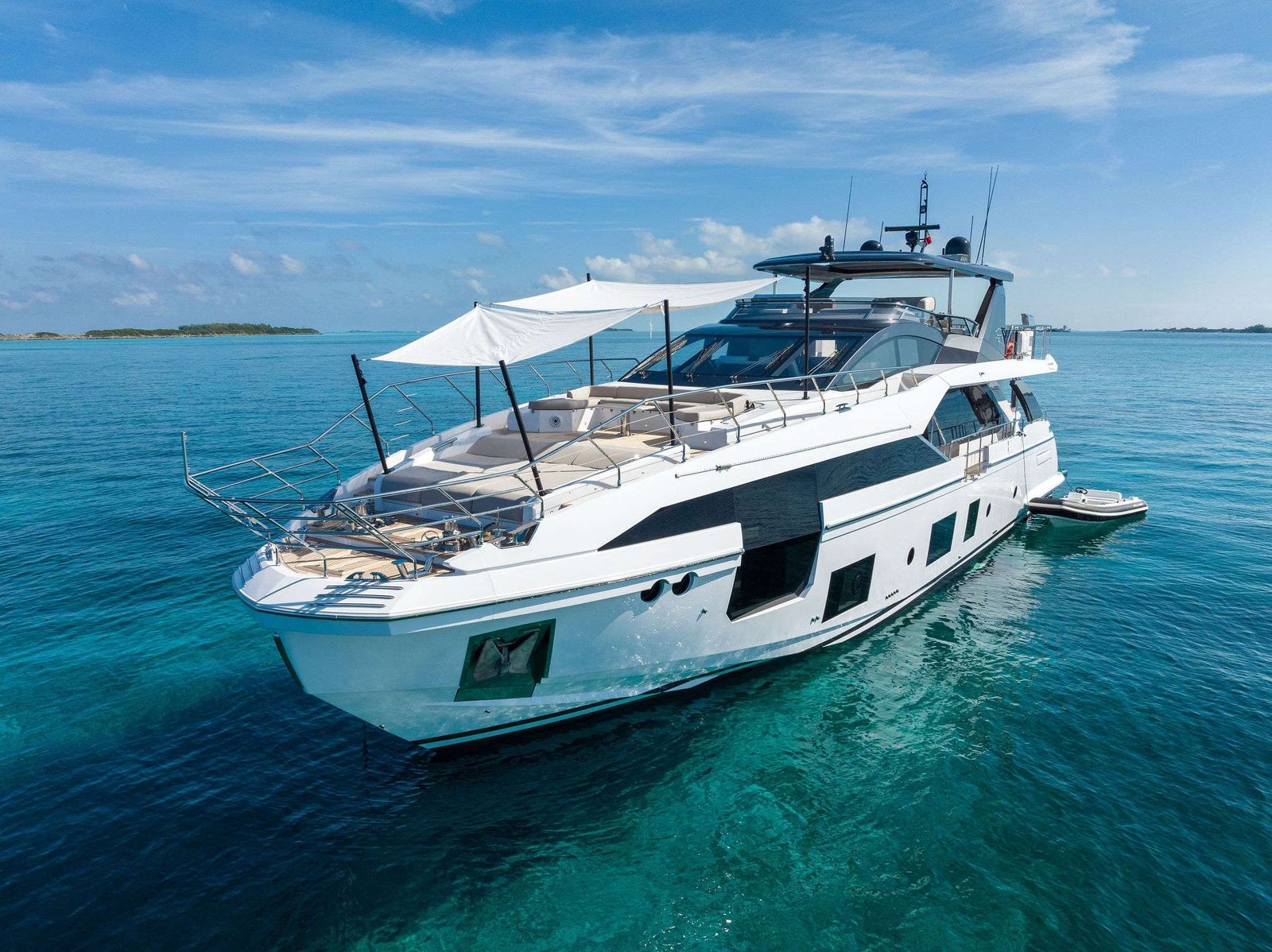 White luxury motor yacht on calm turquoise ocean under a blue sky, with a distant shoreline.
