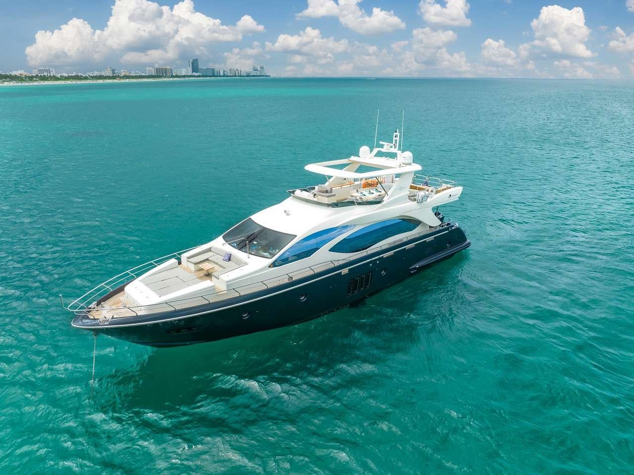 White luxury motor yacht cruising on turquoise sea with a distant city skyline on the horizon.