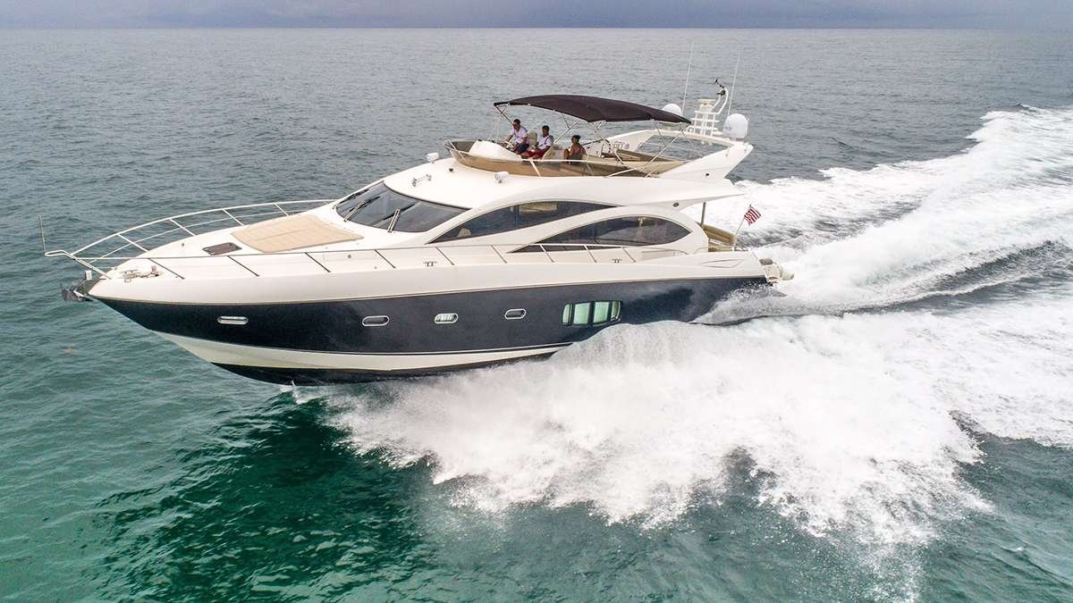 White luxury motor yacht speeding across turquoise sea with people on the upper deck under a canopy.