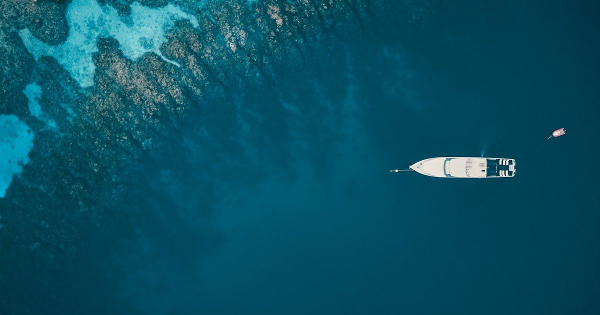 Aerial view of a single yacht anchored in turquoise Caribbean water off Roatán — quiet financial calculations behind a charter booking