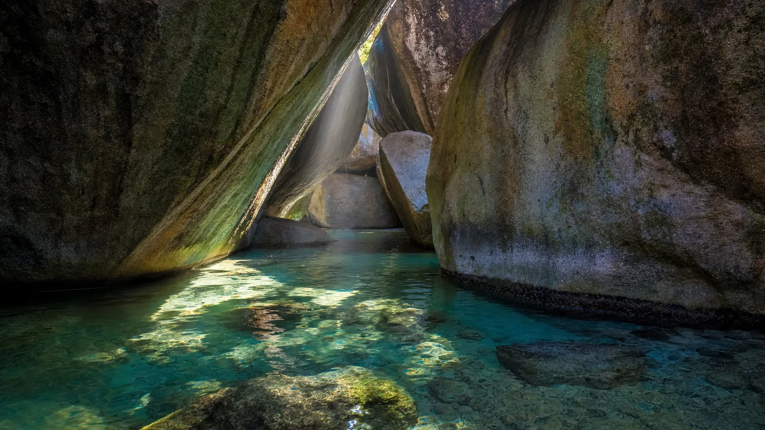Shafts of sunlight falling through giant granite boulders onto a clear sea pool inside the grotto popularly called the Cathedral Room at The Baths on Virgin Gorda