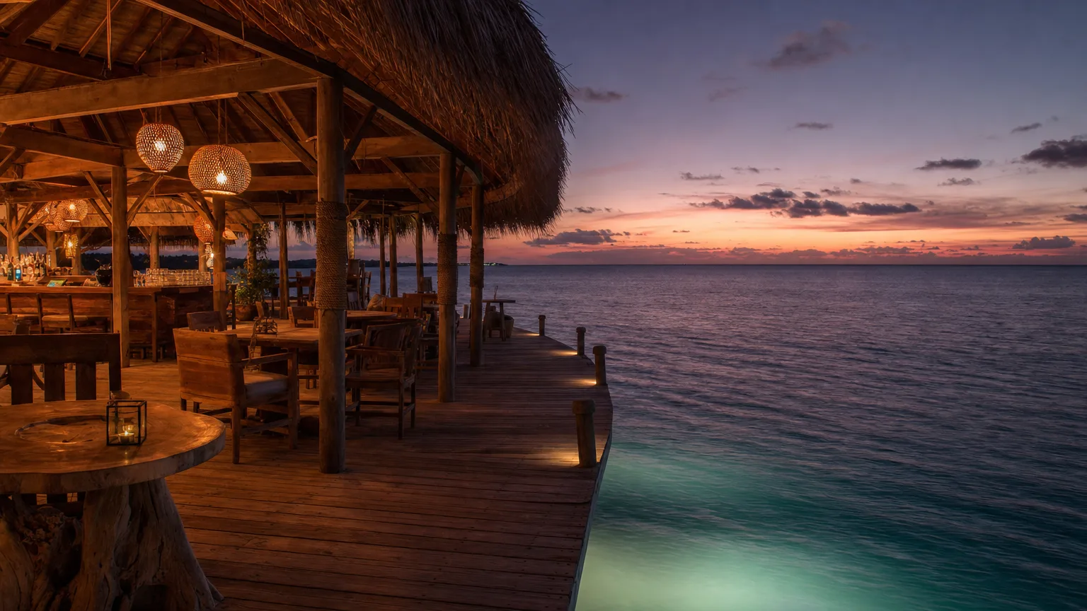 Basil's Bar overwater deck at dusk on Mustique with lanterns, thatched roof and calm sea below