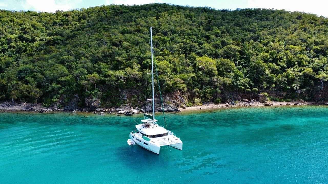 White catamaran anchored near a rocky, forested shoreline with clear turquoise water.