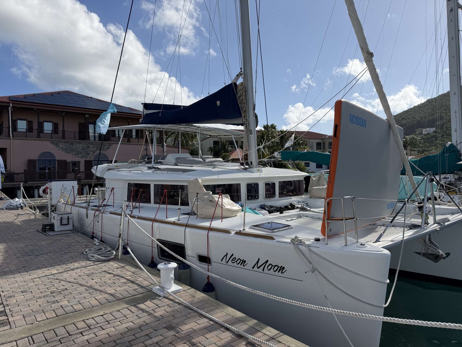 Sailboat moored at a marina with tall masts and rigging, the boat named Neon Moon on its hull.