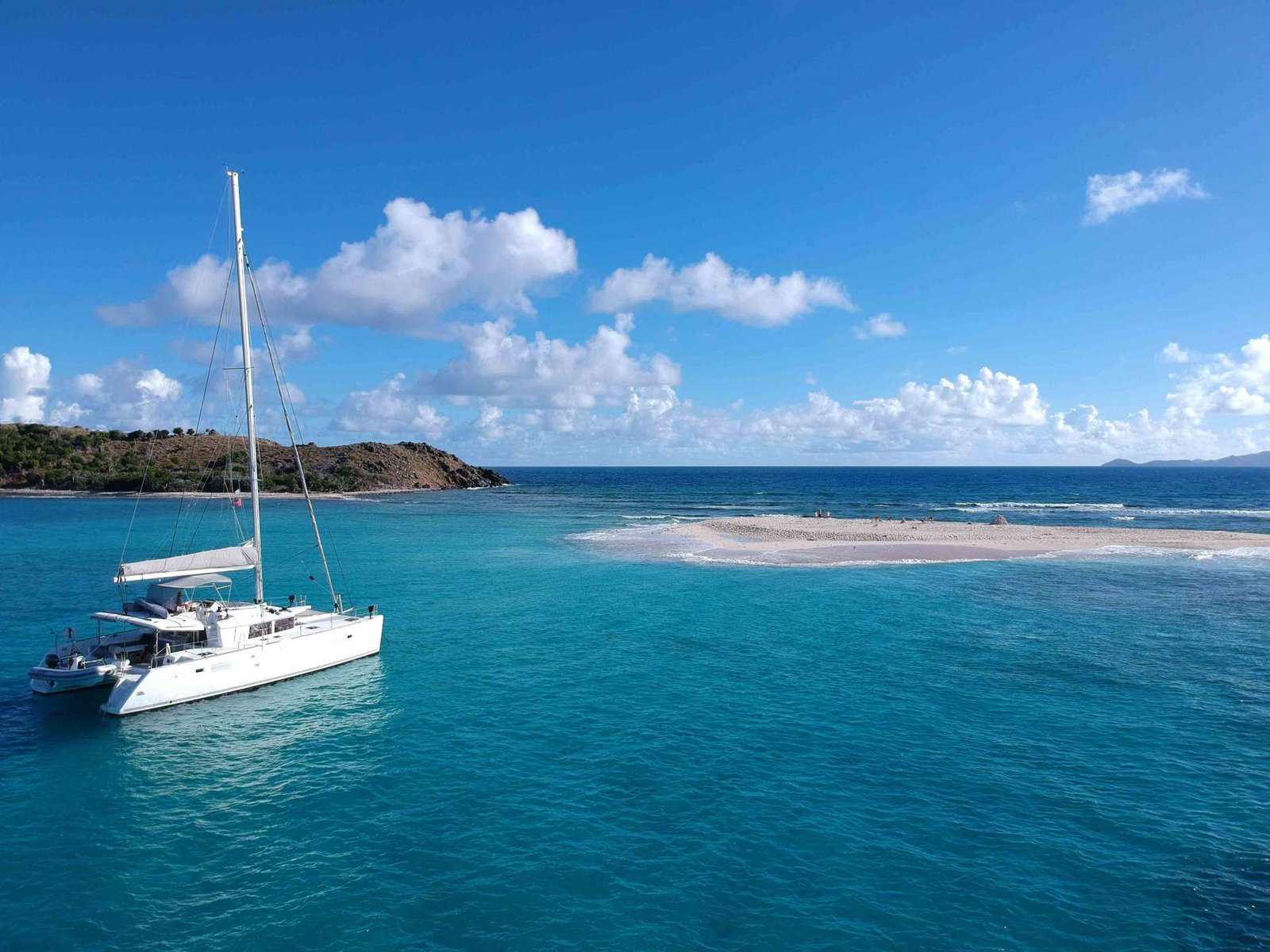 White sailing catamaran near a sandy beach with turquoise water and a clear blue sky from a coastal scene.