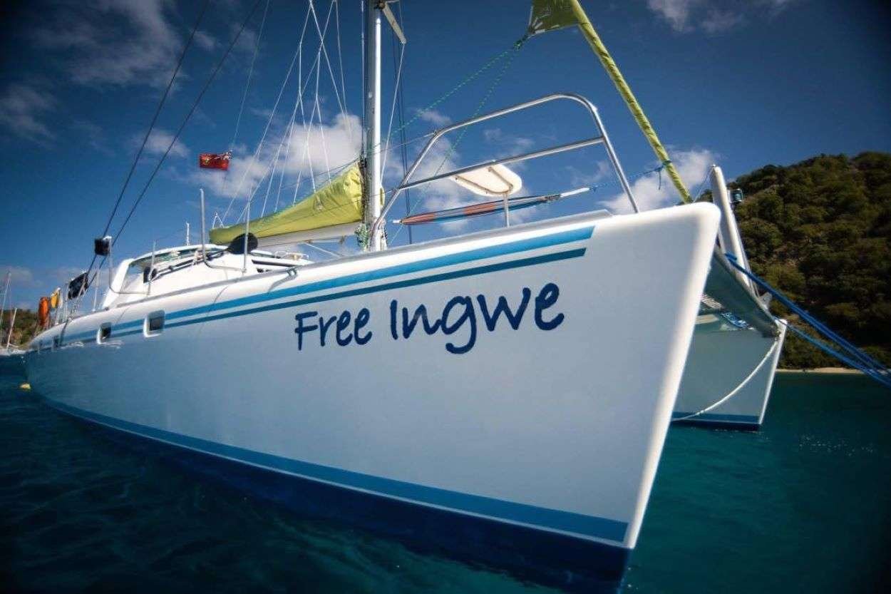 Sailboat named 'Free Ingwe' anchored in clear blue water with rigging and sails visible in a sunny scene.