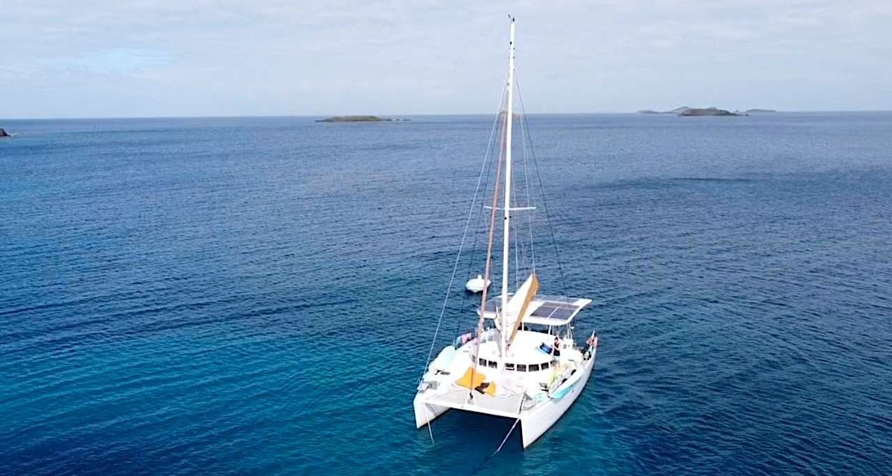 White catamaran anchored in turquoise blue water with small islands on the horizon.