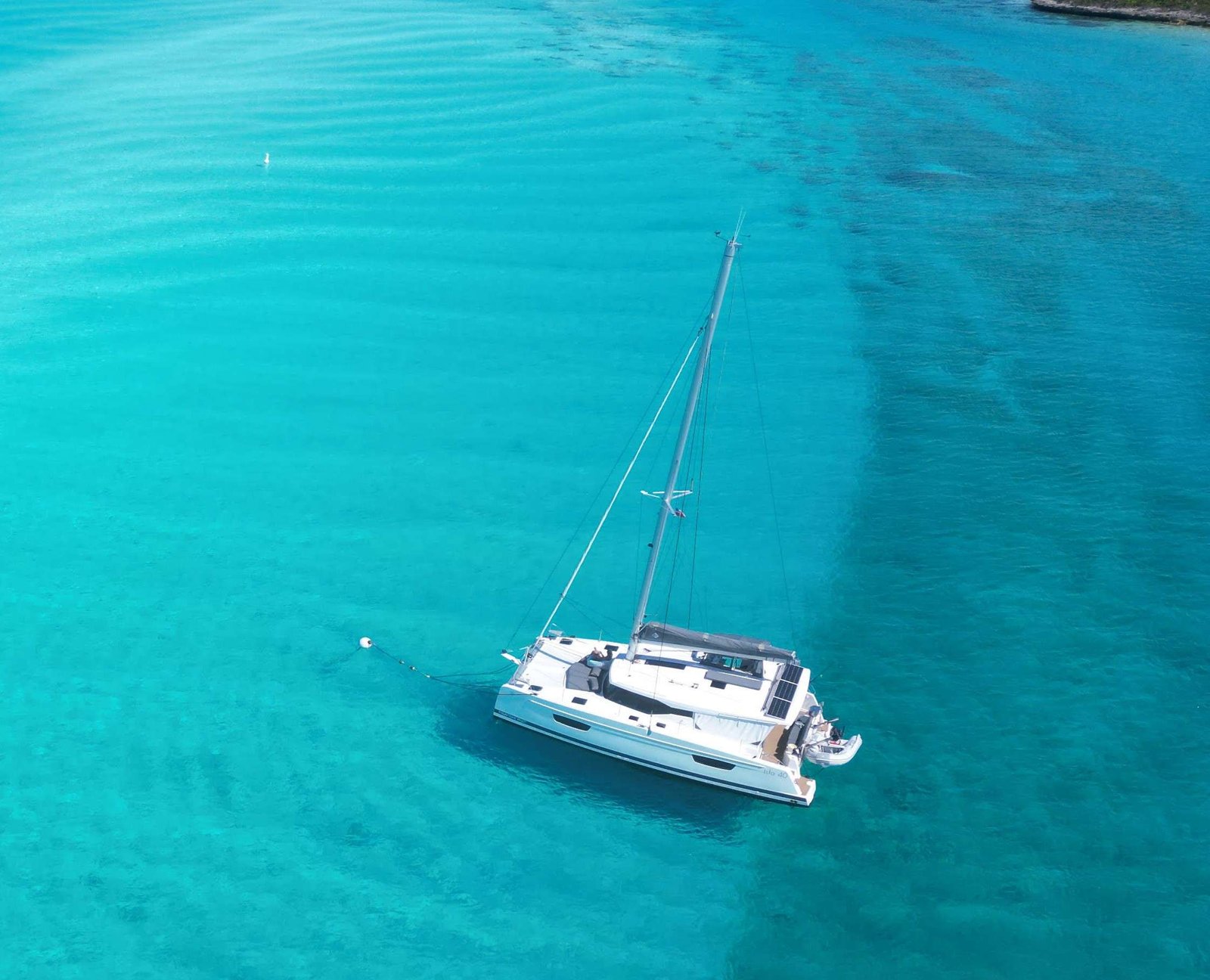 A white sailing yacht on bright turquoise sea, viewed from above (aerial view)./ Aerial view of a white sailboat anchored in crystal-clear blue-green water.