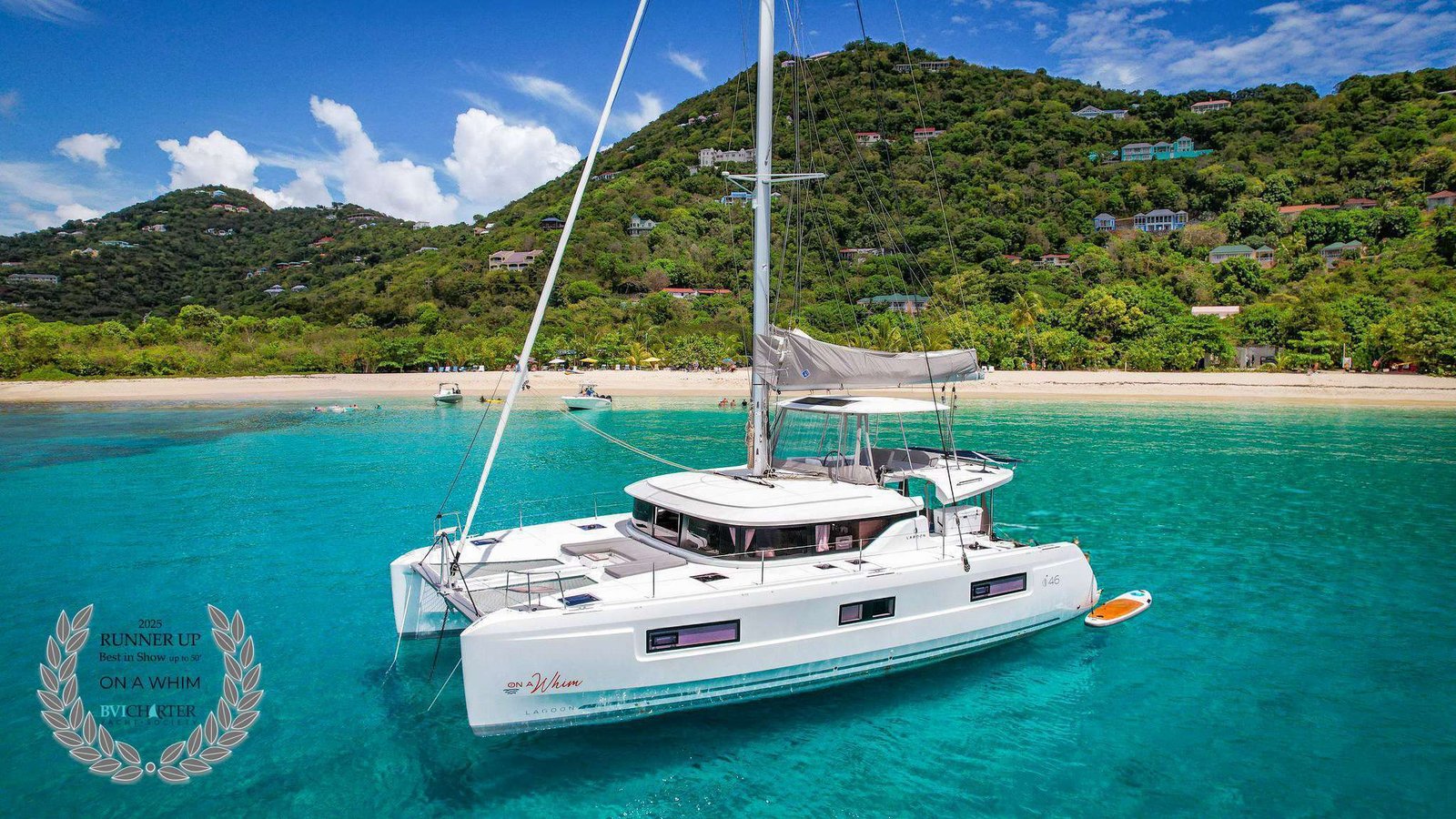 White catamaran yacht anchored in clear turquoise water with a sandy beach and lush green hills in the background.
