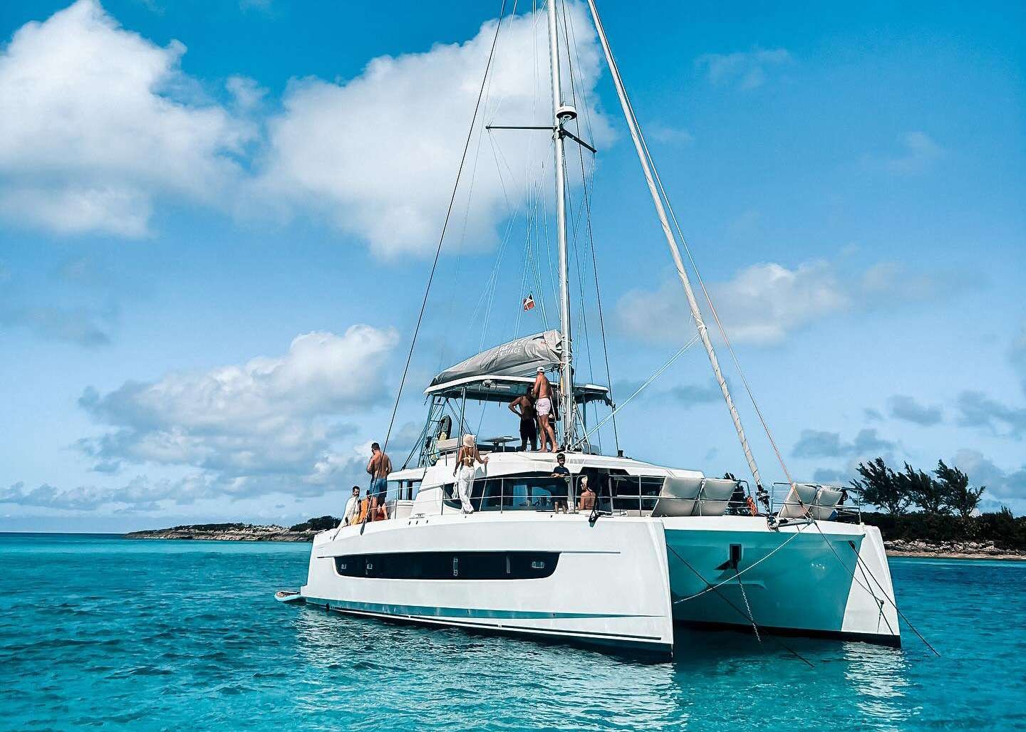 White catamaran sailing/anchored in turquoise sea with people on deck under a bright blue sky sea breeze.