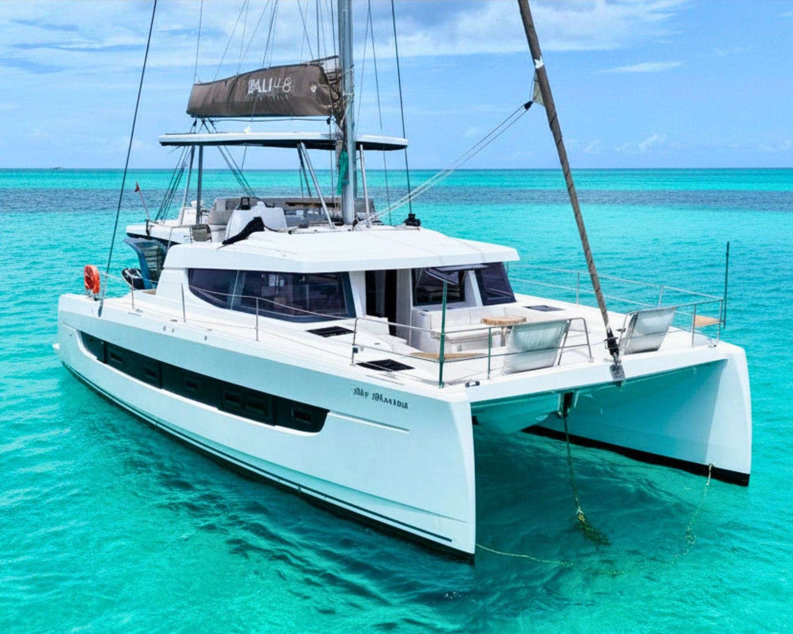 White catamaran yacht anchored in turquoise tropical waters with a clear blue sky above.
