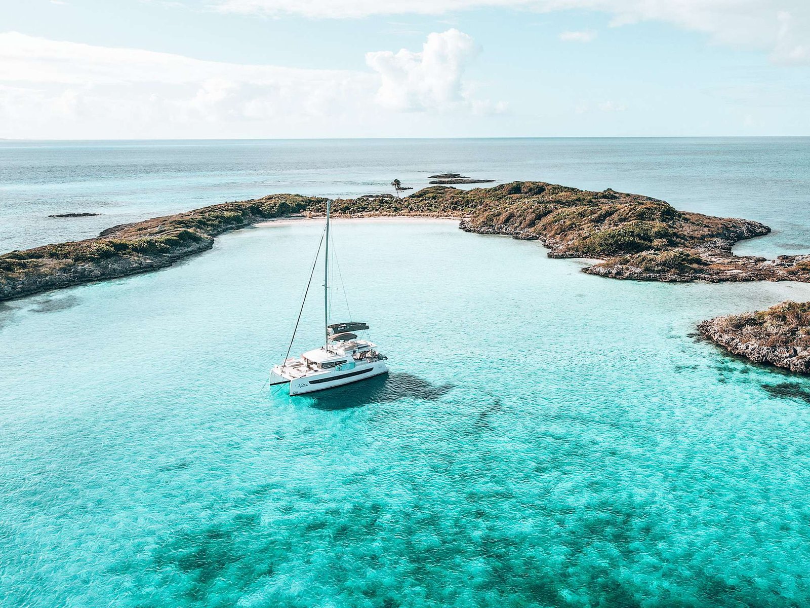 White sailboat anchored in a turquoise lagoon near a rocky tropical shoreline with a small palm tree.