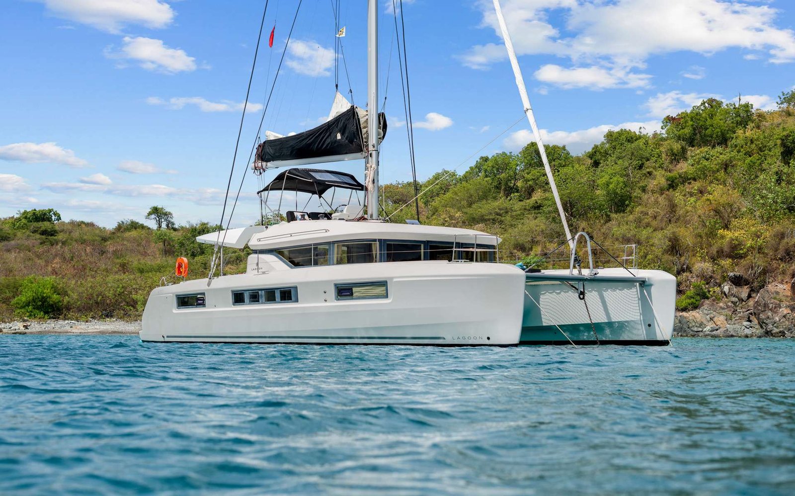 White Lagoon catamaran anchored near a rocky, green coastline under a blue sky with scattered clouds.