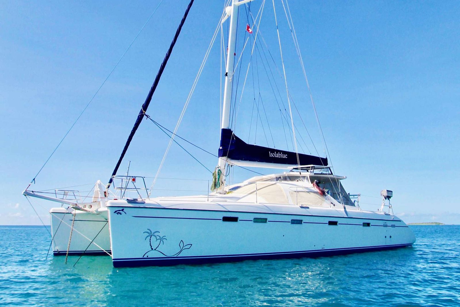 White sailing yacht anchored in clear blue water, with tall mast and rigging against a bright sky.