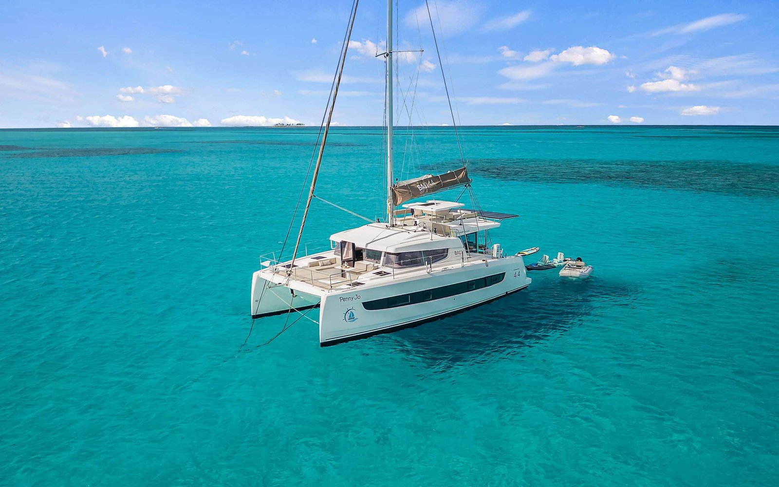 White sailing catamaran Penny Jo moored in turquoise Caribbean waters under a sunny blue sky.