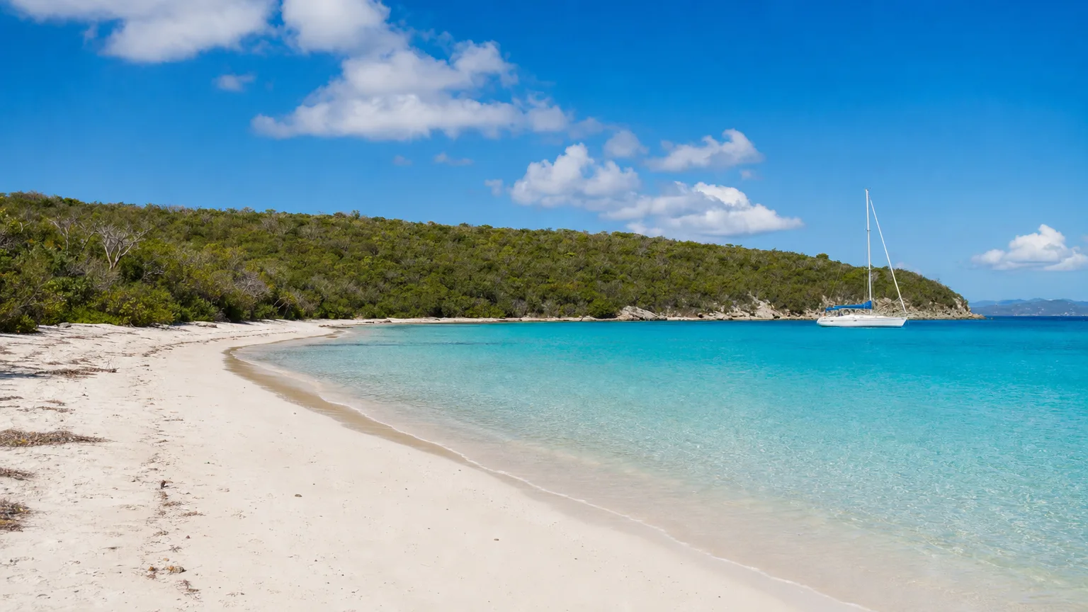 Quiet white sand West Beach on Buck Island, an uninhabited Caribbean island, with a sailboat anchored offshore