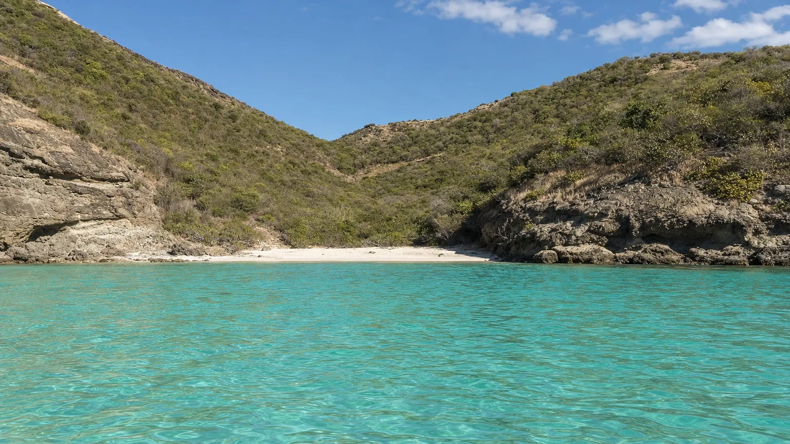 Île Fourchue seen from the water, a bare green island with a sand beach at the head of its bay