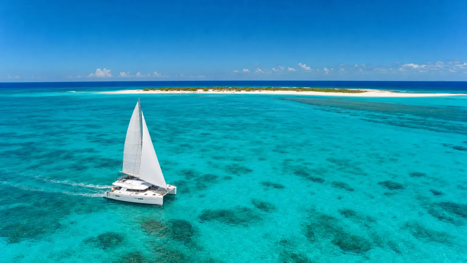 A charter yacht approaching low-lying Anegada across the turquoise water inside Horseshoe Reef