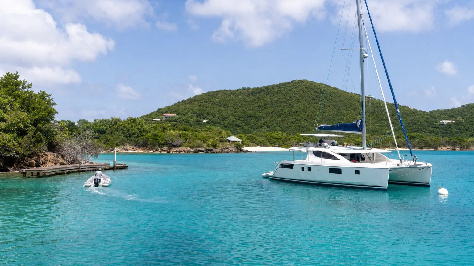 Crewed catamaran moored off a small green Caribbean cay with a tender running toward a dock in the US Virgin Islands