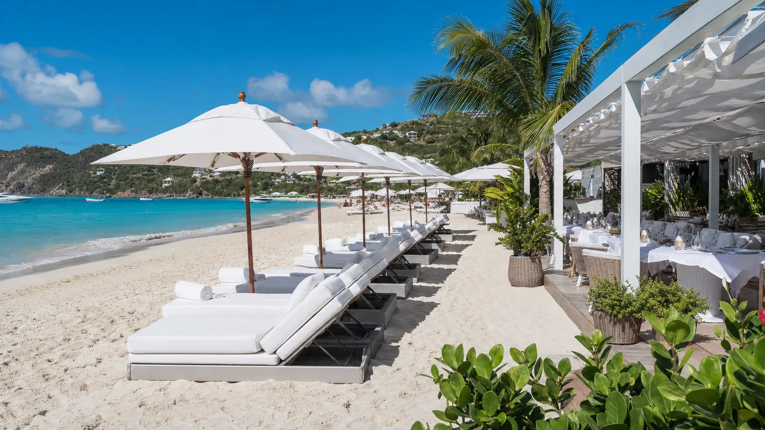 Chic beach club with all-white sun beds and umbrellas on a turquoise St. Barts bay with al fresco dining