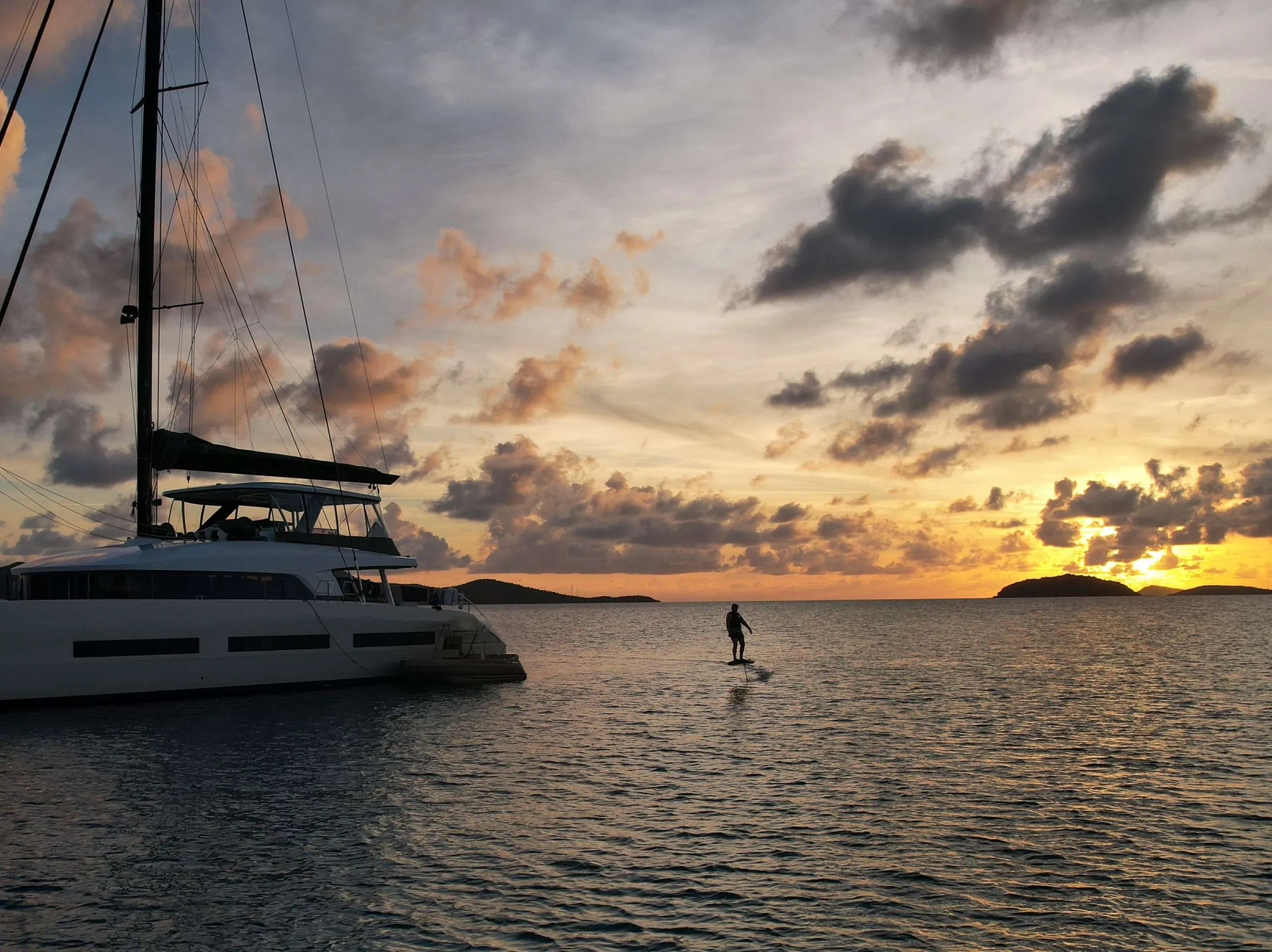 Guest riding an eFoil at sunset beside the catamaran AEOLUS