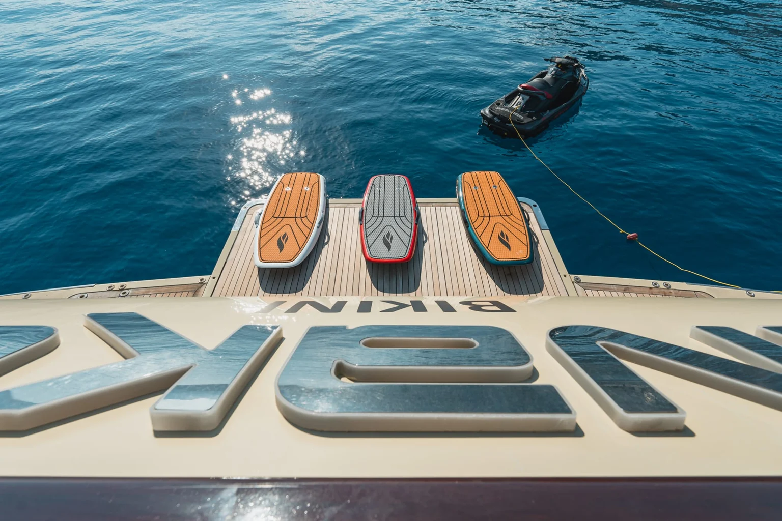 Three SiFly eFoil boards lined up on a yacht's teak swim platform with a jet ski tied off astern