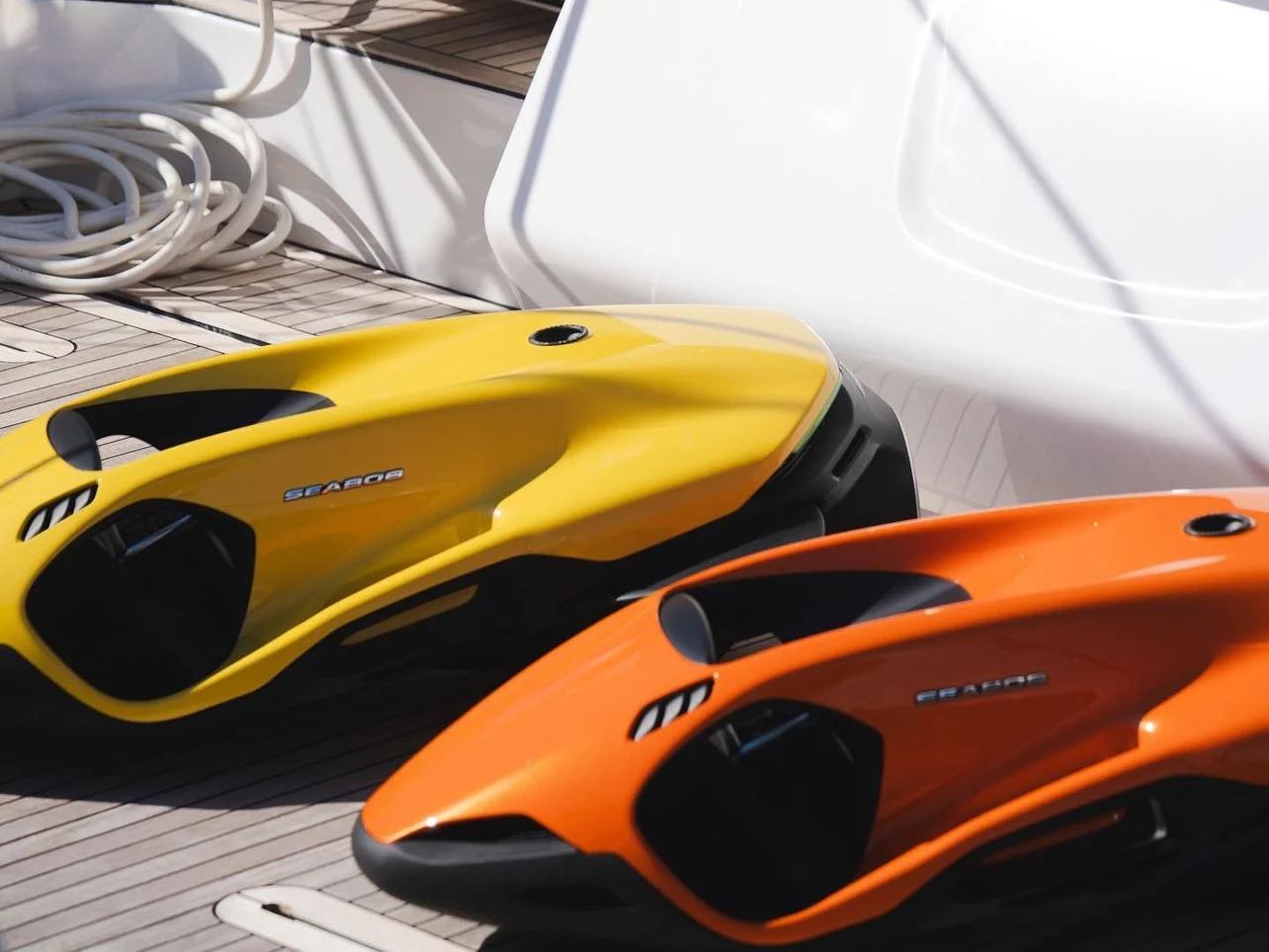 A yellow and an orange SEABOB F9 resting on the teak aft deck of a charter yacht