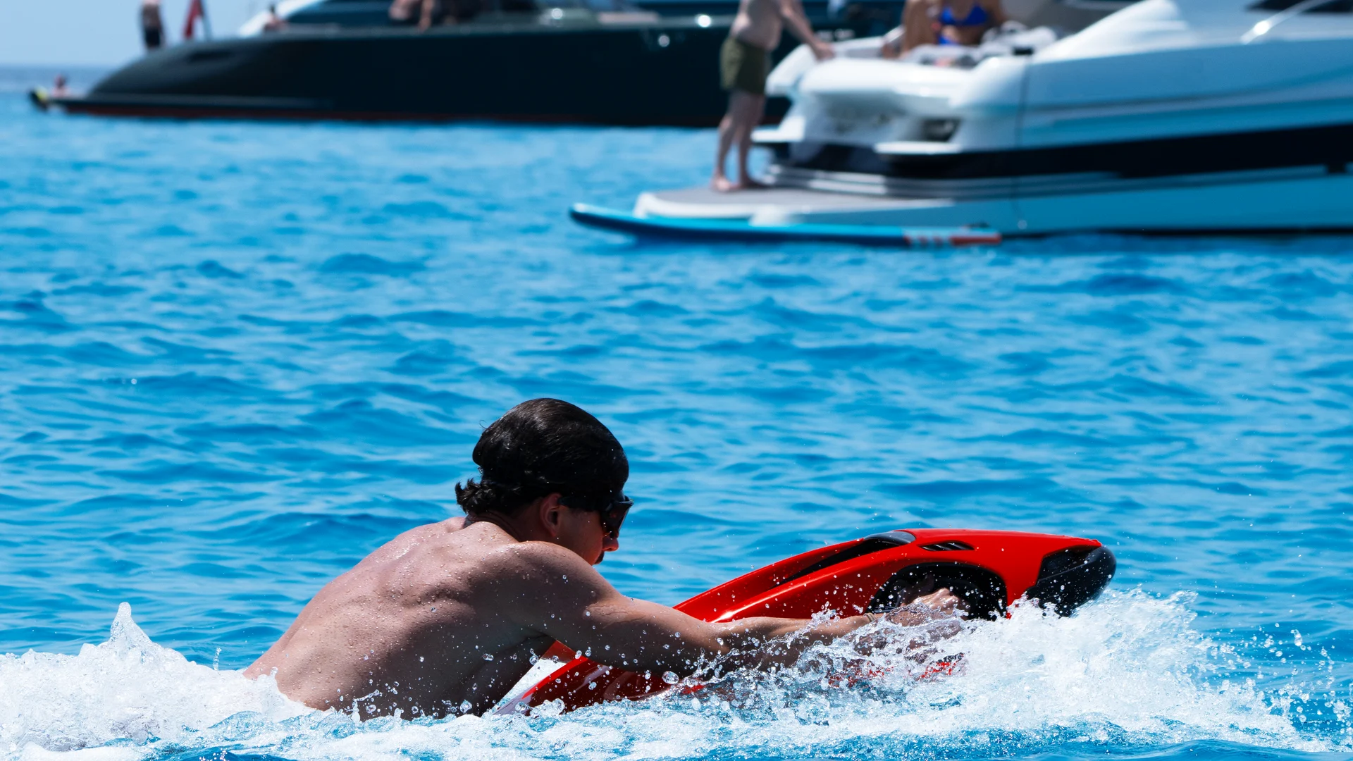 SEABOB F9 ridden past yachts at anchor | Vital Charters Charter yachts with a SEABOB: a rider on a red SEABOB F9 passes motor yachts at anchor