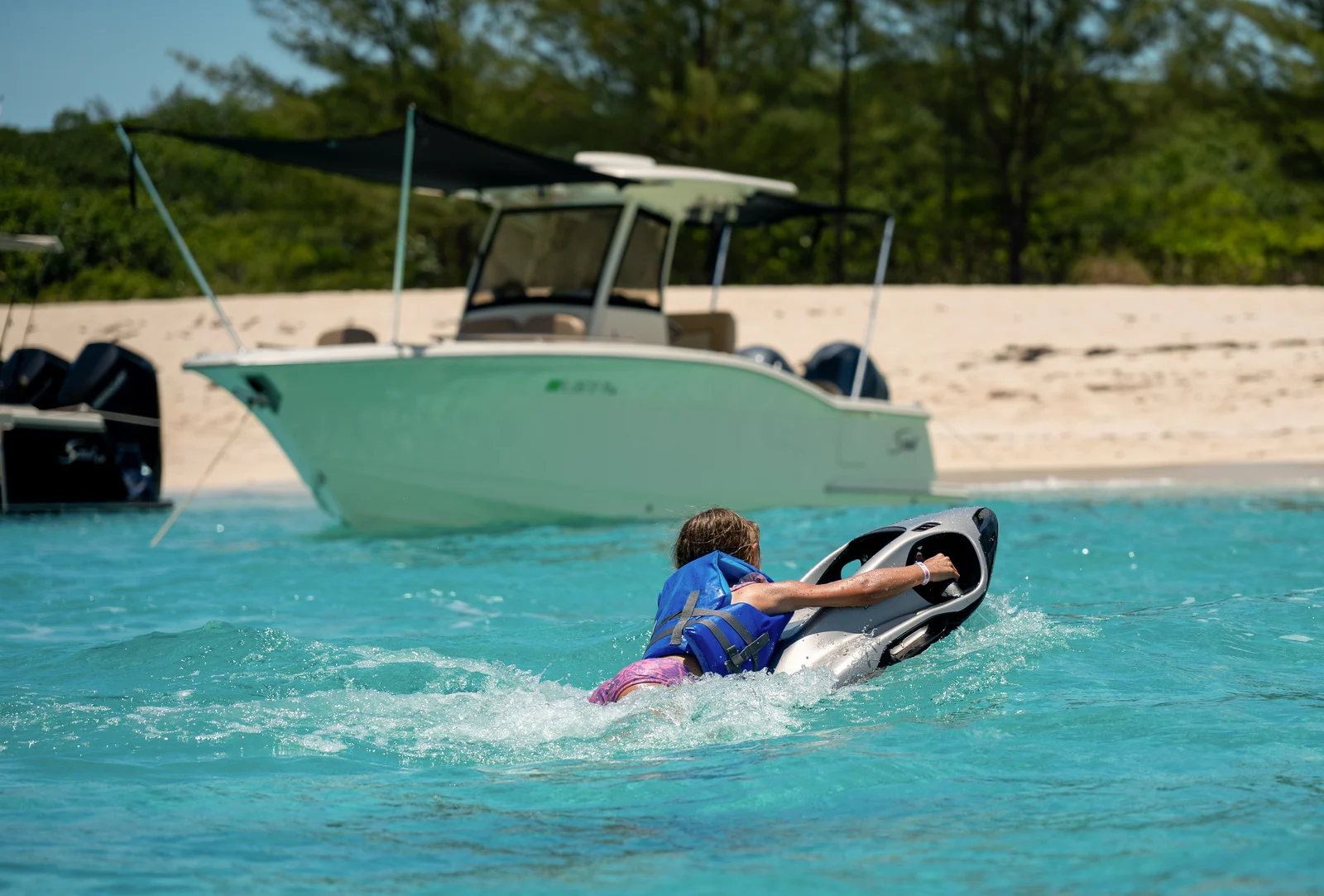 A young rider in a flotation vest on a SEABOB in calm, shallow turquoise water off a beach